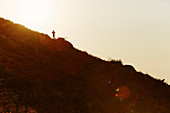 Silhouette of runner ascending hillside at sunset