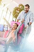 Father pushing daughter on luggage cart in airport
