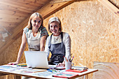 Smiling artists with laptop and drawings in studio