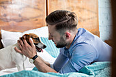 Man petting Jack Russell Terrier on bed
