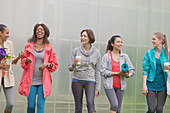 Smiling women walking with yoga mats and coffee