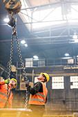 Steel workers looking up at crane chain in factory