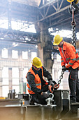 Steel workers fastening crane chain to steel