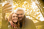 Smiling couple taking selfie under autumn tree