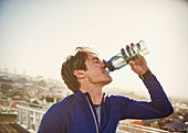 Male runner drinking water on urban footbridge