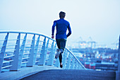 Male runner running on urban footbridge at dawn