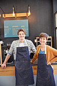 Portrait smiling cafe owners wearing denim aprons