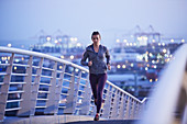 Female runner running on urban footbridge at dawn