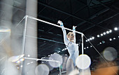 Female gymnast with arms raised below uneven bars