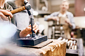 Jeweller using hammer and equipment in workshop