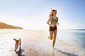 Young woman and dog running on sunny beach