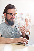 Male designer drinking coffee working at laptop