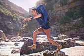 Young man with backpack hiking, jumping rocks