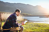 Young man using tablet at lakeside