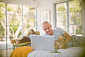 Smiling man with dog using laptop on bed