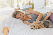 Portrait woman relaxing, petting dog on bed