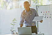 Male doctor with paperwork standing at laptop