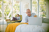 Mature couple relaxing, using laptop and tablet