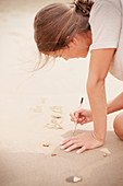 Teenage girl with stick writing in sand