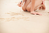 Girl with pencil writing in sand on summer beach