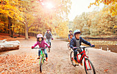 Young family bike riding along pond in autumn park