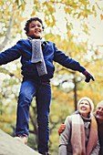 Grandparents watching boy on log in autumn woods