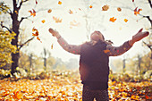 Playful girl throwing leaves overhead in park
