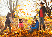 Young family playing in autumn leaves in park