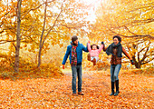 Parents swinging daughter in autumn park
