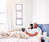 Smiling couple relaxing, reading book in bed