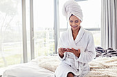Smiling woman in bathrobe using tablet on bed
