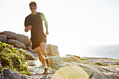 Male triathlete running on rocky trail along ocean