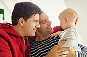 Affectionate male gay parents cuddling baby son