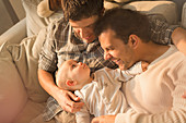 Male gay parents cuddling with baby son