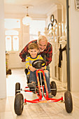 Father pushing son on toy car in foyer corridor