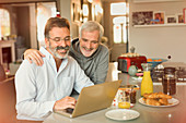 Male gay couple using laptop and eating breakfast