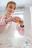 Smiling woman baking, cracking egg over bowl