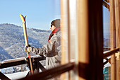 Male skier with skis on sunny cabin balcony