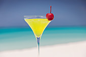 Close up yellow cocktail with cherry on beach