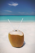 Coconut with two straws on ocean beach