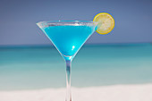 Blue cocktail with lemon slice on ocean beach