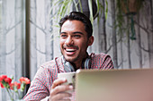 Man laughing and drinking coffee at laptop
