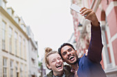 Laughing young couple taking selfie in city