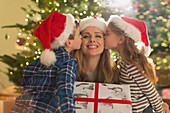 Daughter and son in Santa hats kissing mother