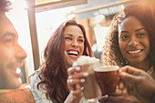 Enthusiastic friends toasting coffee cups at cafe