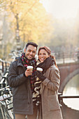 Young couple drinking coffee along autumn canal