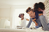 Multi-ethnic daughters tackling father on bed