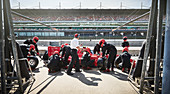 Manager and pit crew replacing tires on race car