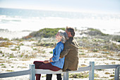 Affectionate senior couple sitting on beach fence