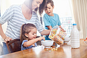 Mother pouring cereal for daughter at breakfast